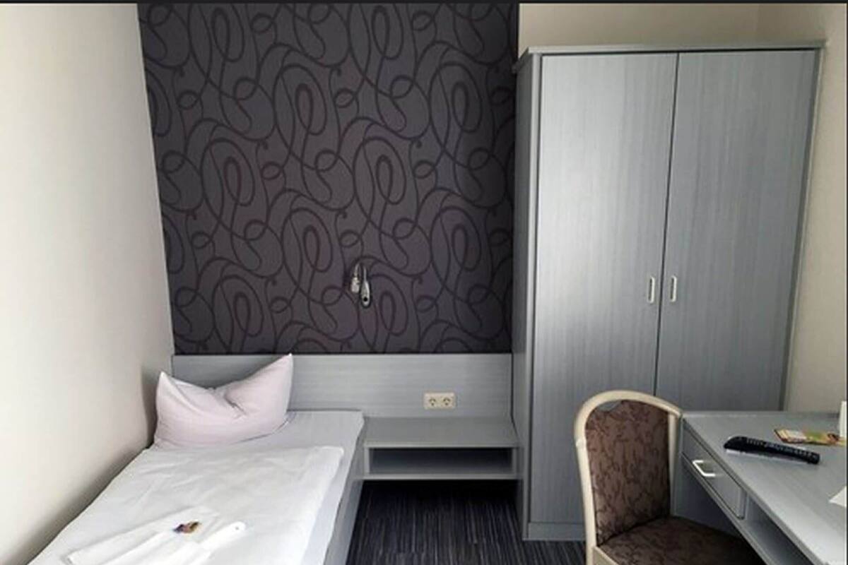 A hotel room with a bed, a desk, a chair, and a wardrobe.