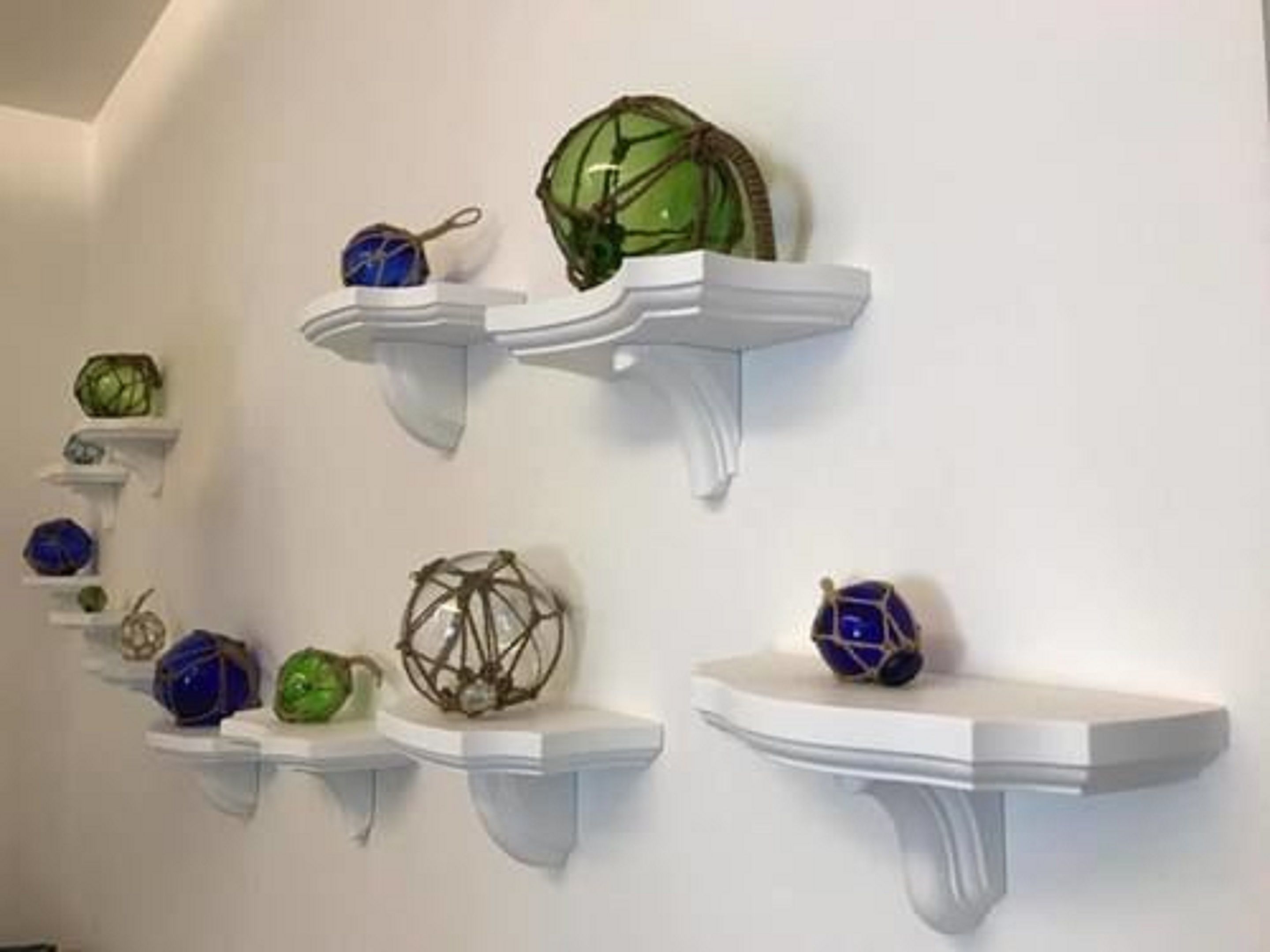 Weiße, an der Wand befestigte Regale mit verschiedenen Glasobjekten.