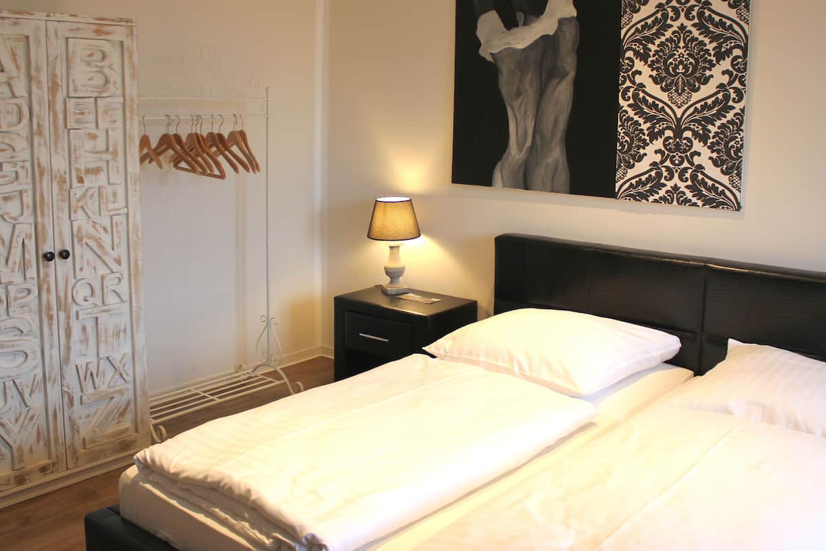 A bedroom with a bed, a nightstand with a lamp, a wardrobe with alphabet letters, and a wall with a black and white pattern.