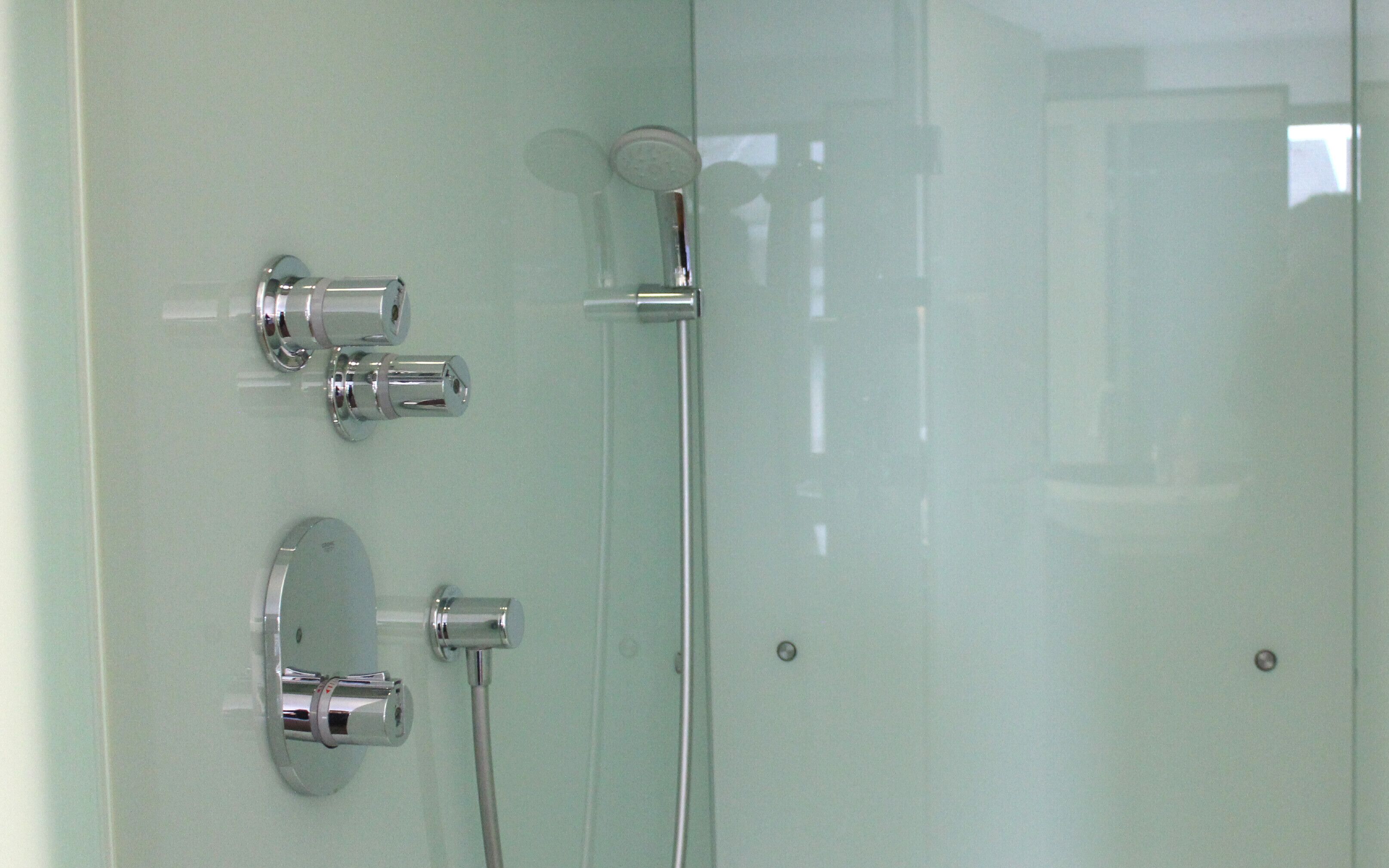 A bathroom with a glass shower enclosure, chrome fixtures, and a visible water control knob.