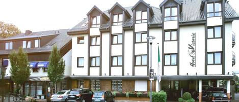 Un hotel con varias habitaciones, un acceso cubierto y un estacionamiento con coches.