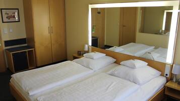 Ein Hotelzimmer mit zwei Einzelbetten, einem großen Spiegel, einem Nachttisch mit Lampe sowie einem kleinen Schreibtisch und einem Stuhl.