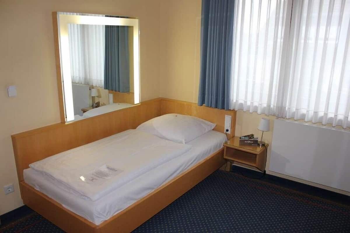 A hotel room with a single bed, a nightstand, a mirror, and a window with curtains.
