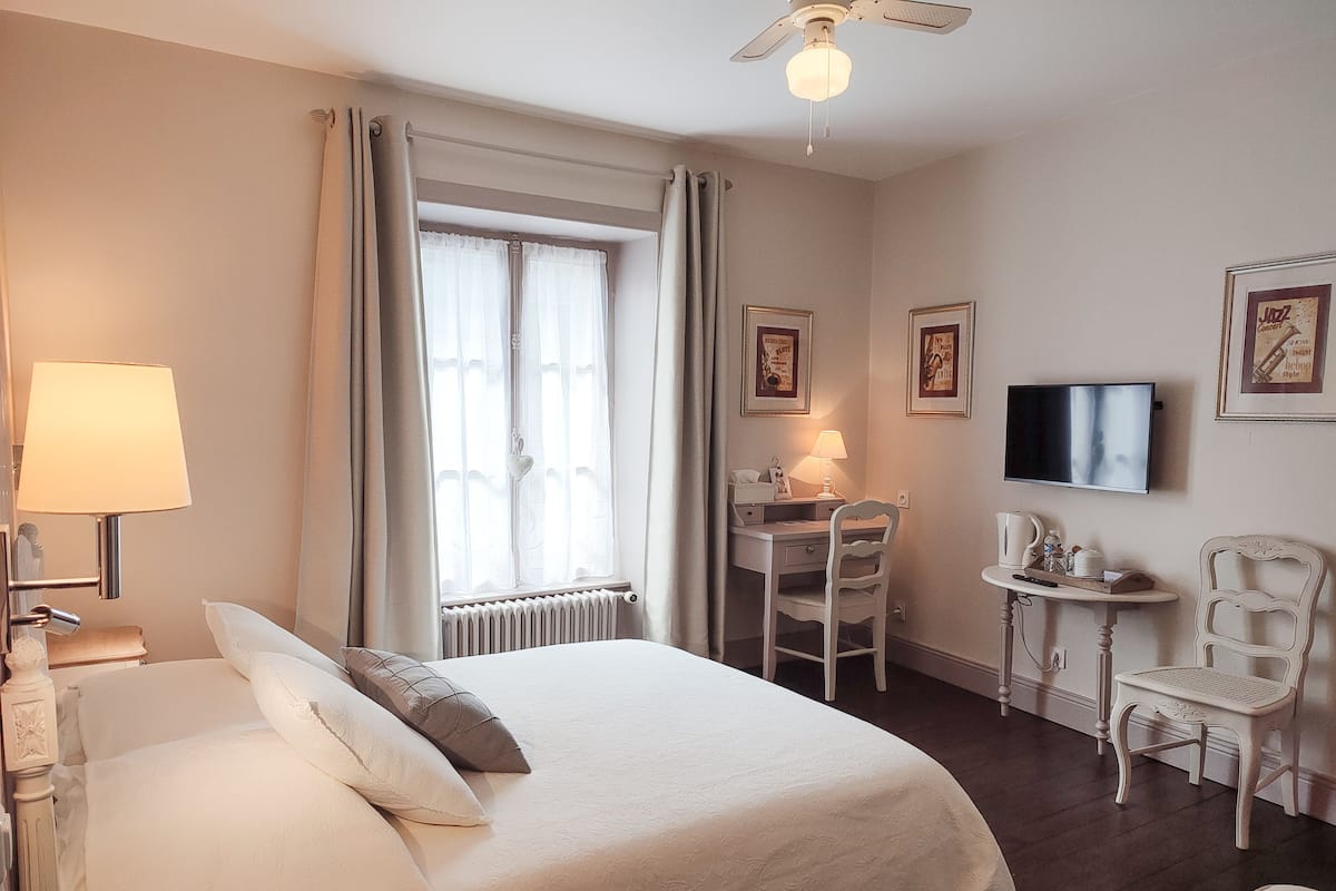 A hotel room with a bed, a desk, a chair, a TV, and a ceiling fan.