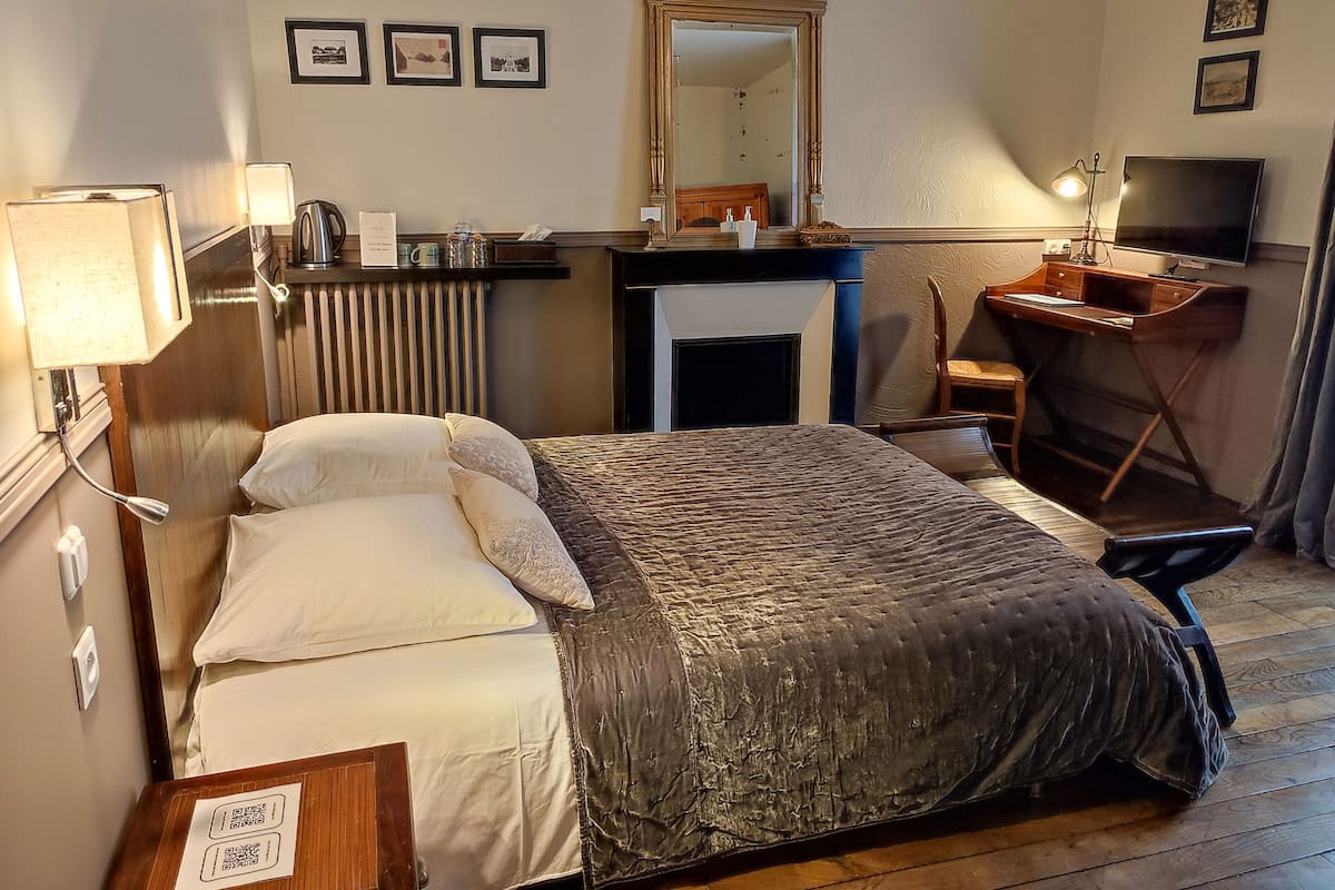 A hotel room with a bed, a desk, a chair, a television, and a mirror.