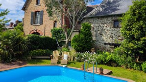 A stone building with a swimming pool, surrounded by lush greenery and two Adirondack chairs. - Le 1900 (Val-Couesnon)