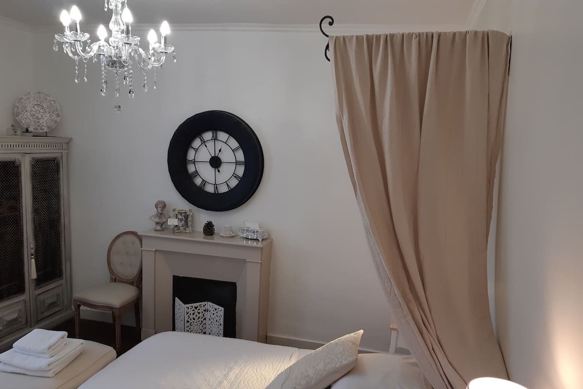 A bedroom with a bed, a chandelier, a clock, a fireplace, and a curtain.