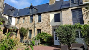 A stone building with a traditional design, featuring multiple windows and a well-maintained garden with outdoor seating. - Le 1900 (Val-Couesnon)