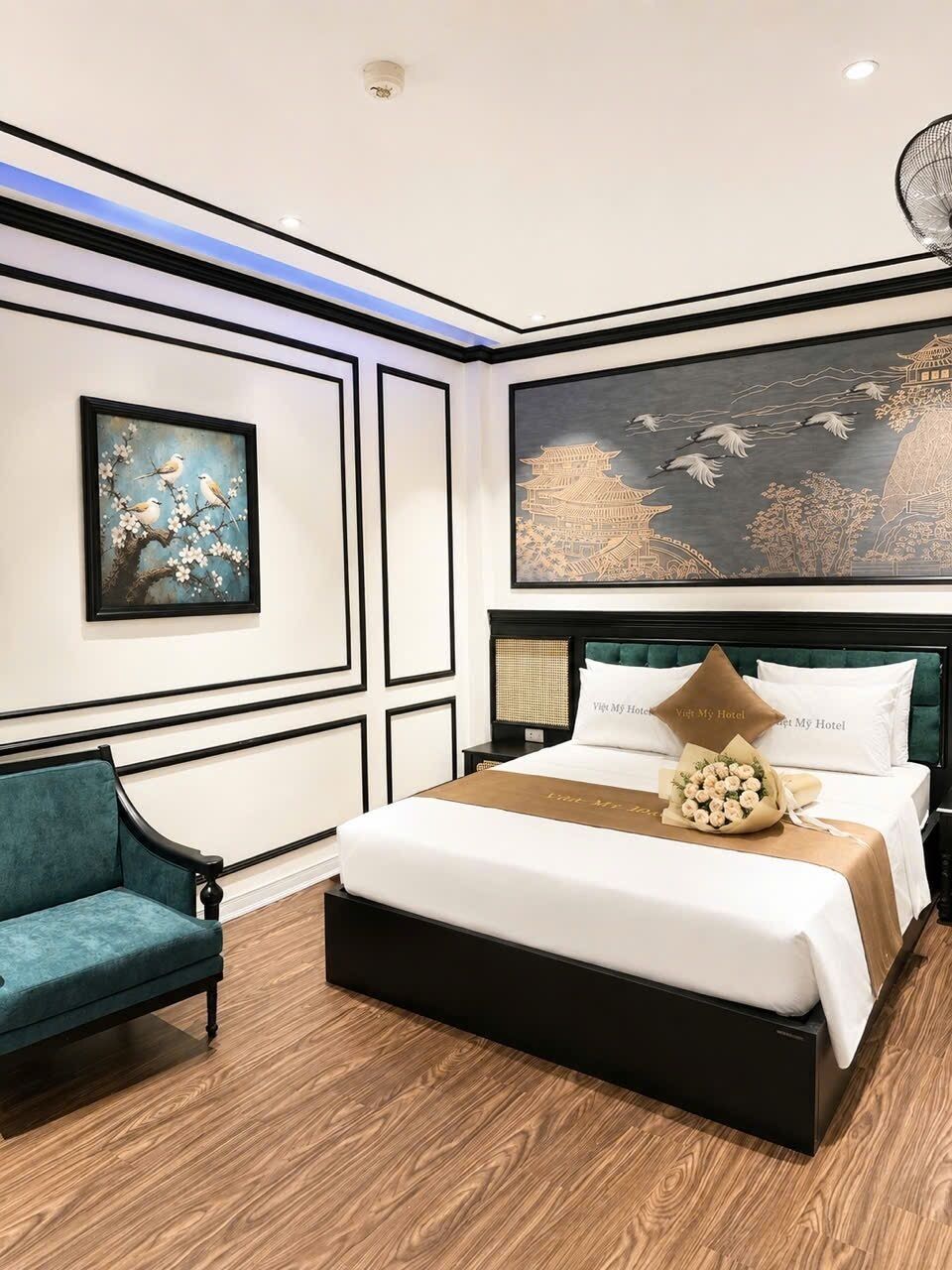 A modern hotel room with a large bed, a blue armchair, and artwork on the walls.