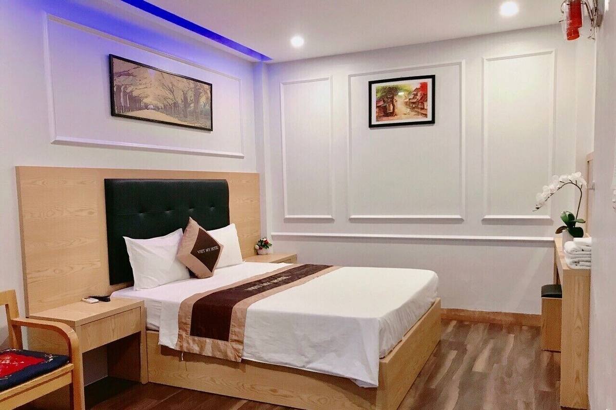 A hotel room with a wooden bed, a nightstand, a chair, and a small table with a plant.