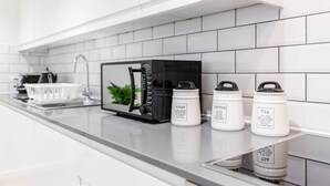 Een moderne keuken met witte kasten, een zwarte magnetron en drie witte bakken met de tekst suiker, koffie en thee.