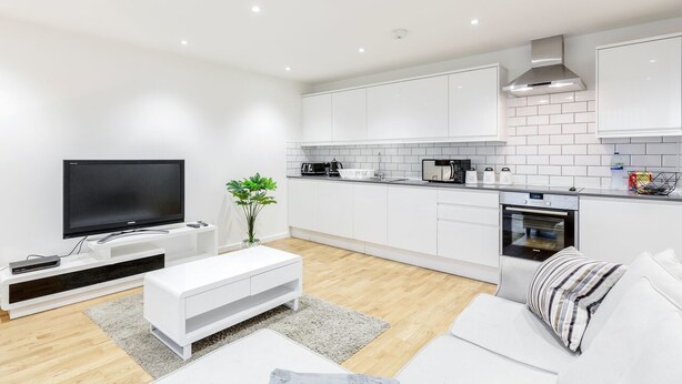 Een moderne keuken met witte kastjes, een ingebouwde oven en een flatscreen televisie.