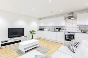 A modern kitchen with white cabinets, a built-in oven, and a flat-screen TV. - Royal Reign Luxury Apartment (Slough)