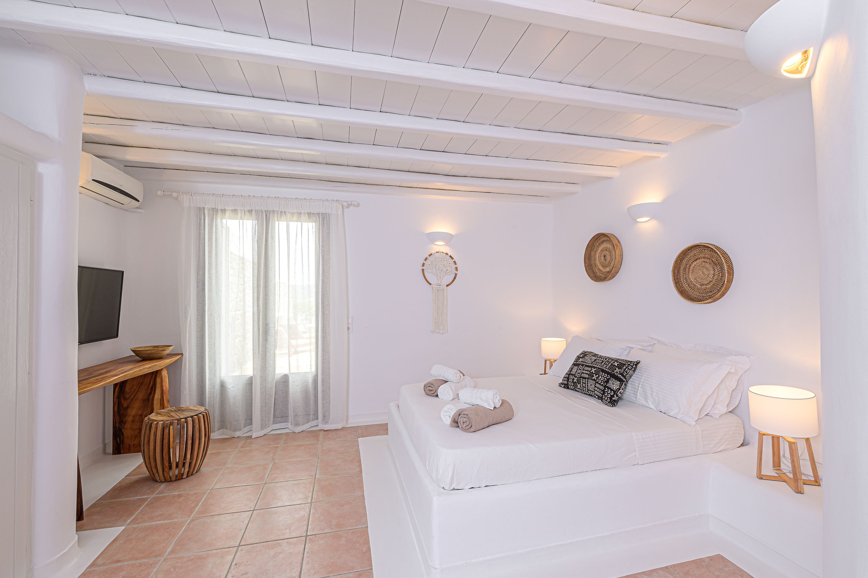 Un dormitorio moderno con cama, lámparas de noche, un televisor y una pequeña mesa de madera.