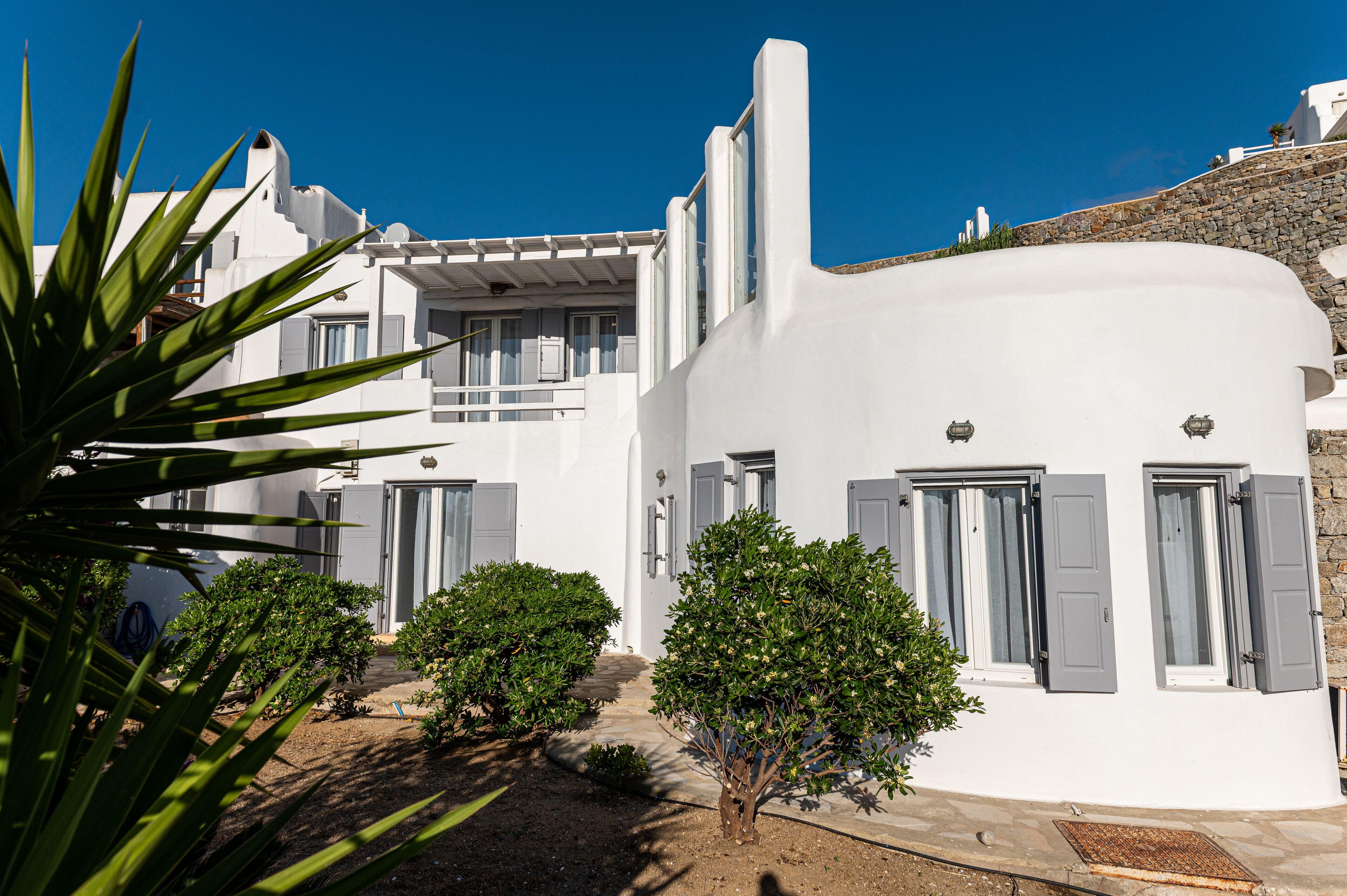 A white building with grey shutters, a stone pathway, and small trees.