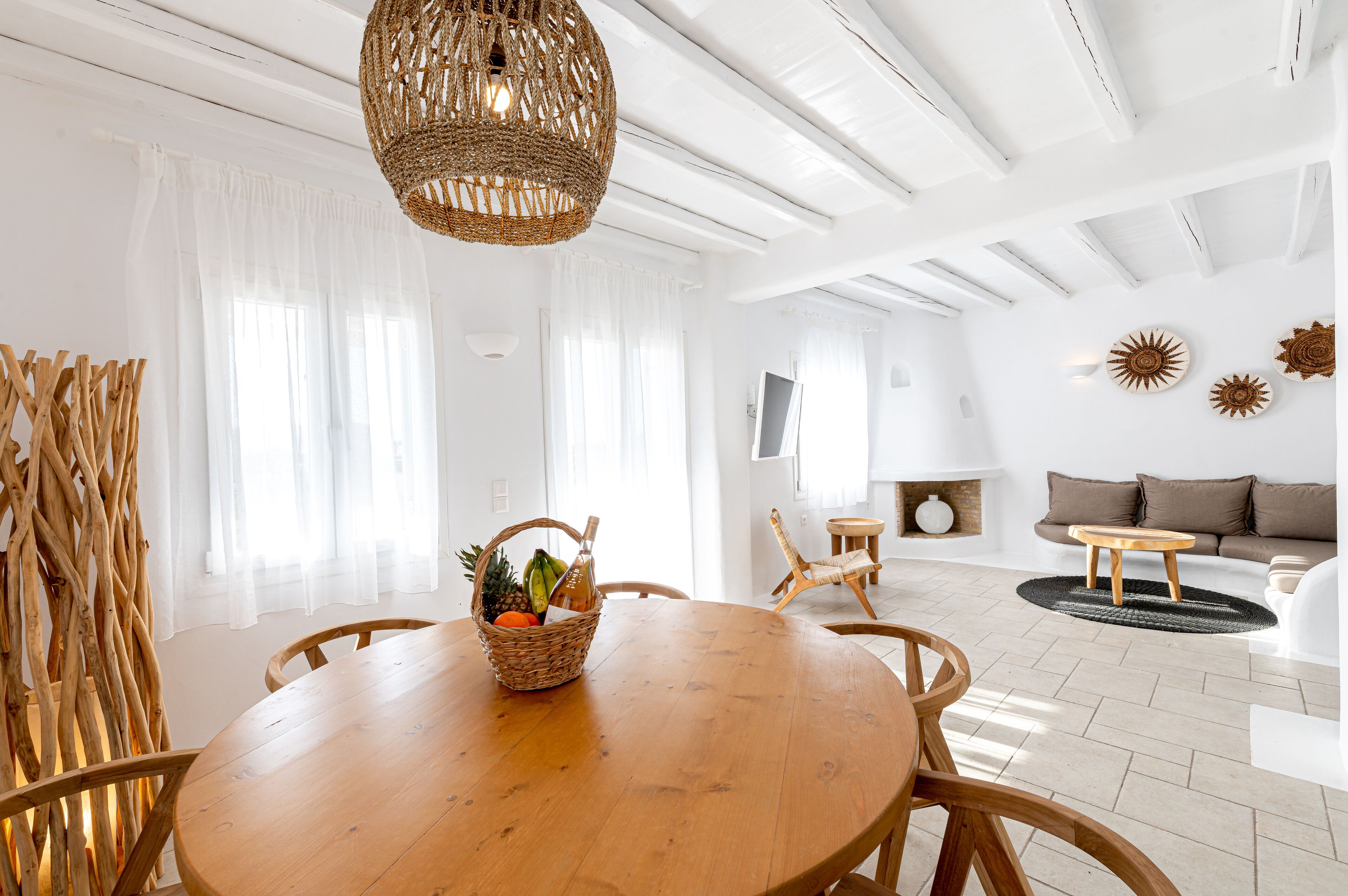 Una habitación luminosa y blanca con una mesa de comedor de madera, una lámpara de techo de mimbre y una silla de mimbre.