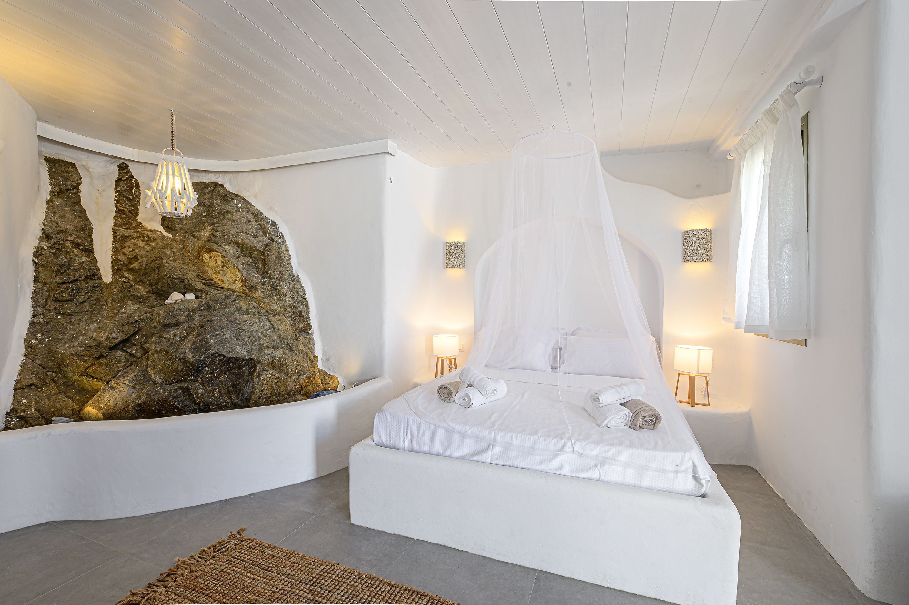 A bedroom with a bed, a large rock wall, and two bedside lamps.