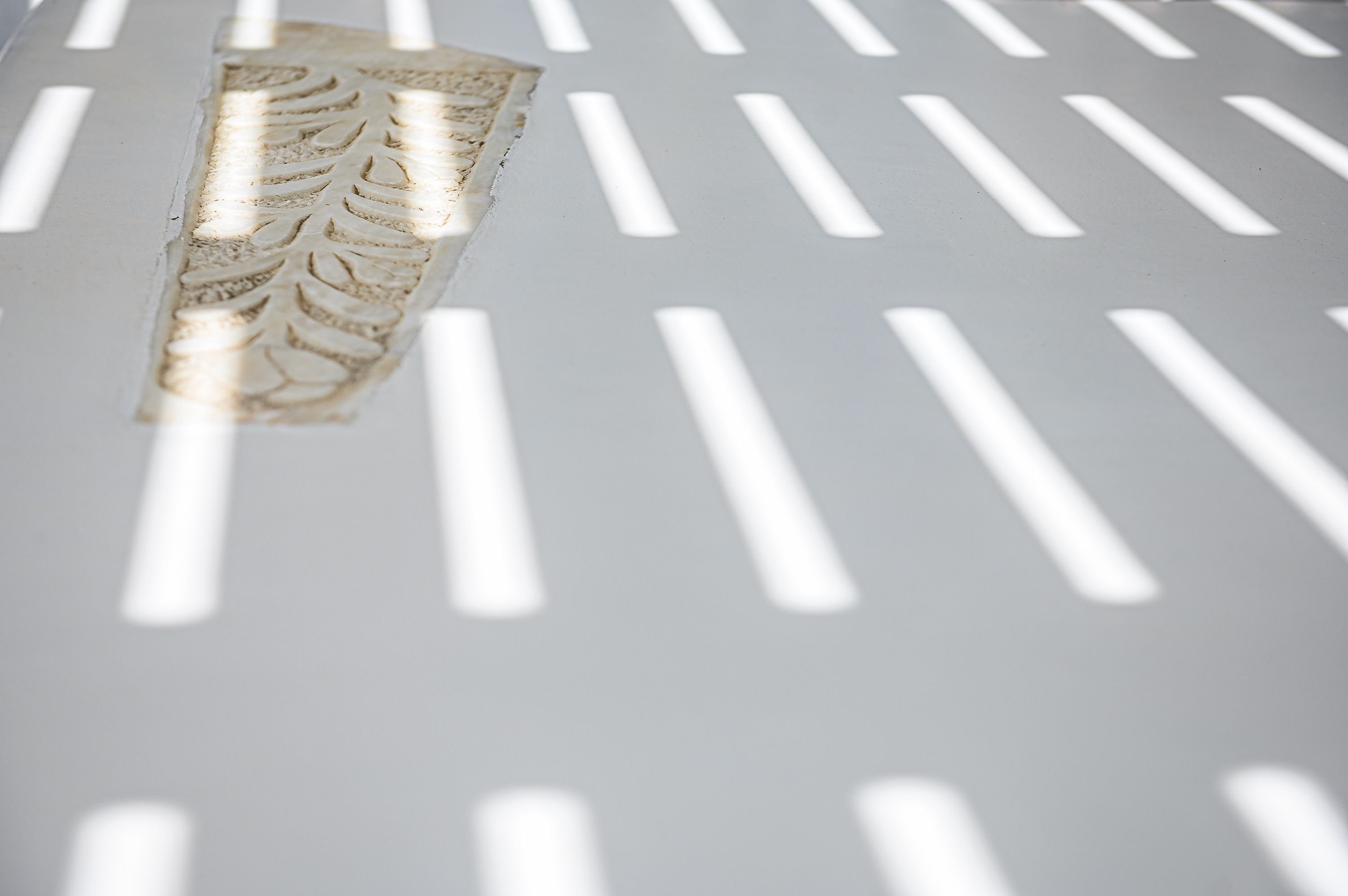 Primer plano de una superficie blanca con textura y listones verticales que proyectan sombras.