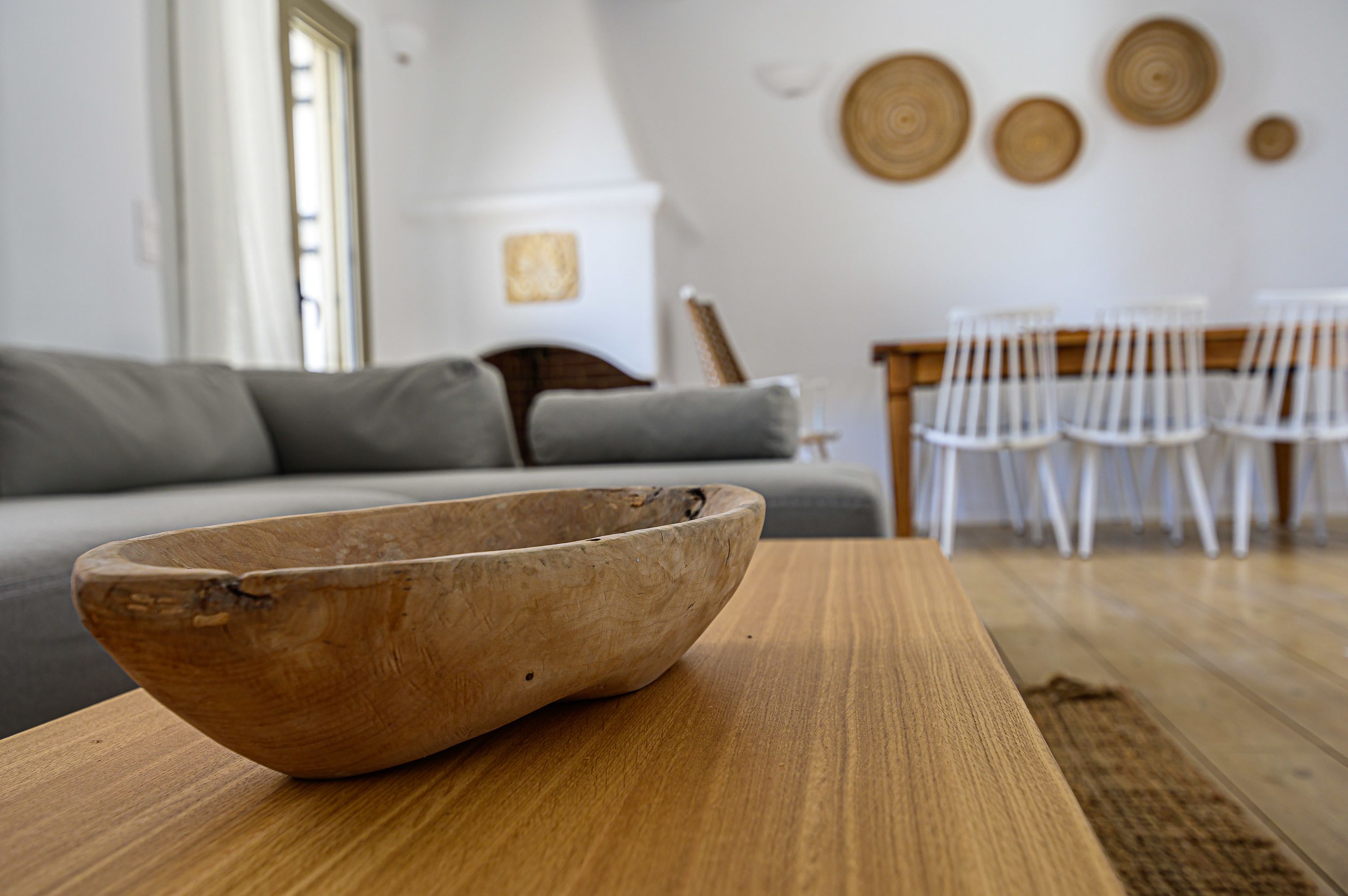 A wooden bowl on a table in a living room with a gray sofa and white chairs.