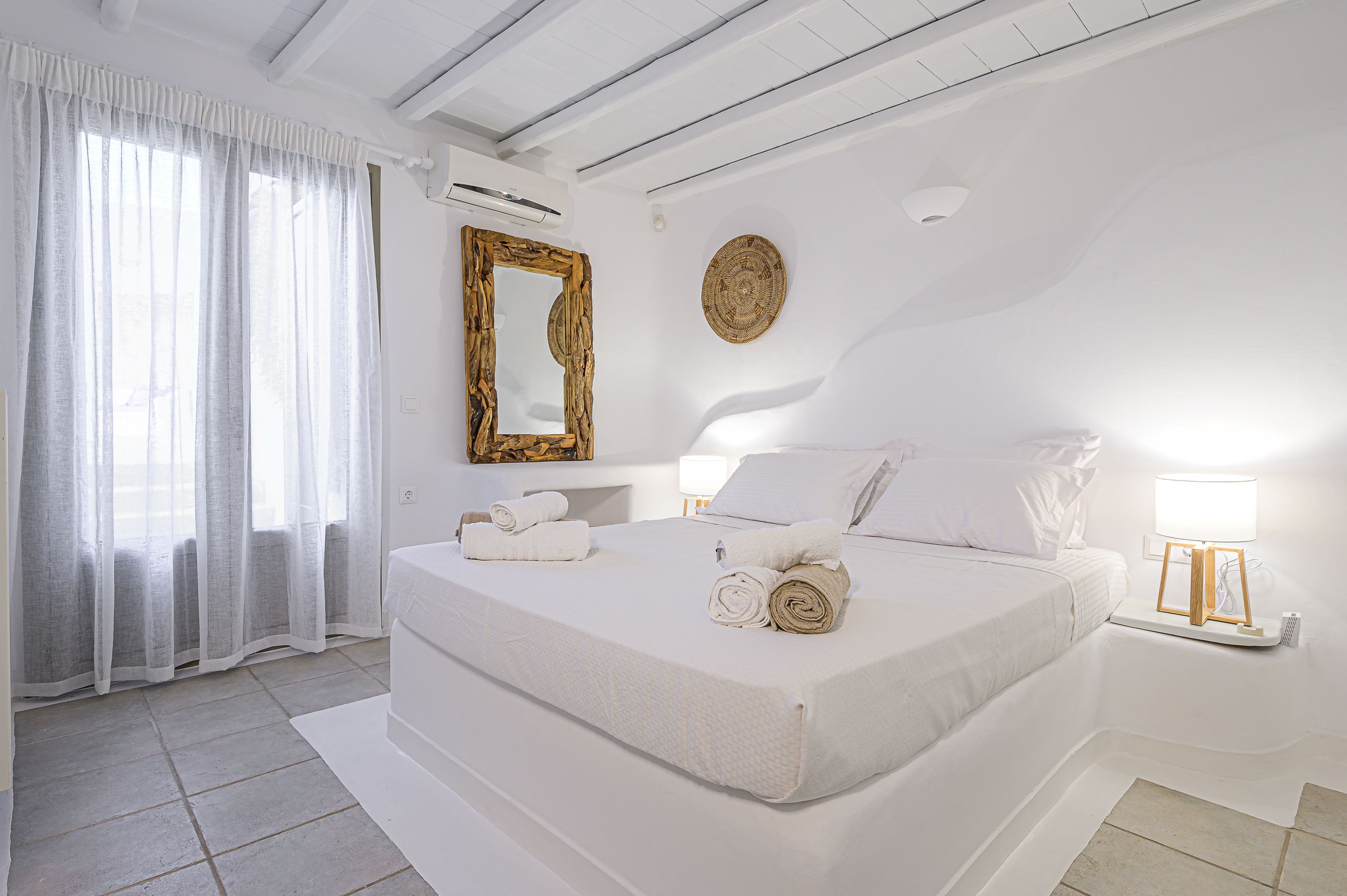 Une chambre moderne avec un grand lit, un miroir à cadre en bois, une table de chevet avec une lampe et un élément décoratif mural.