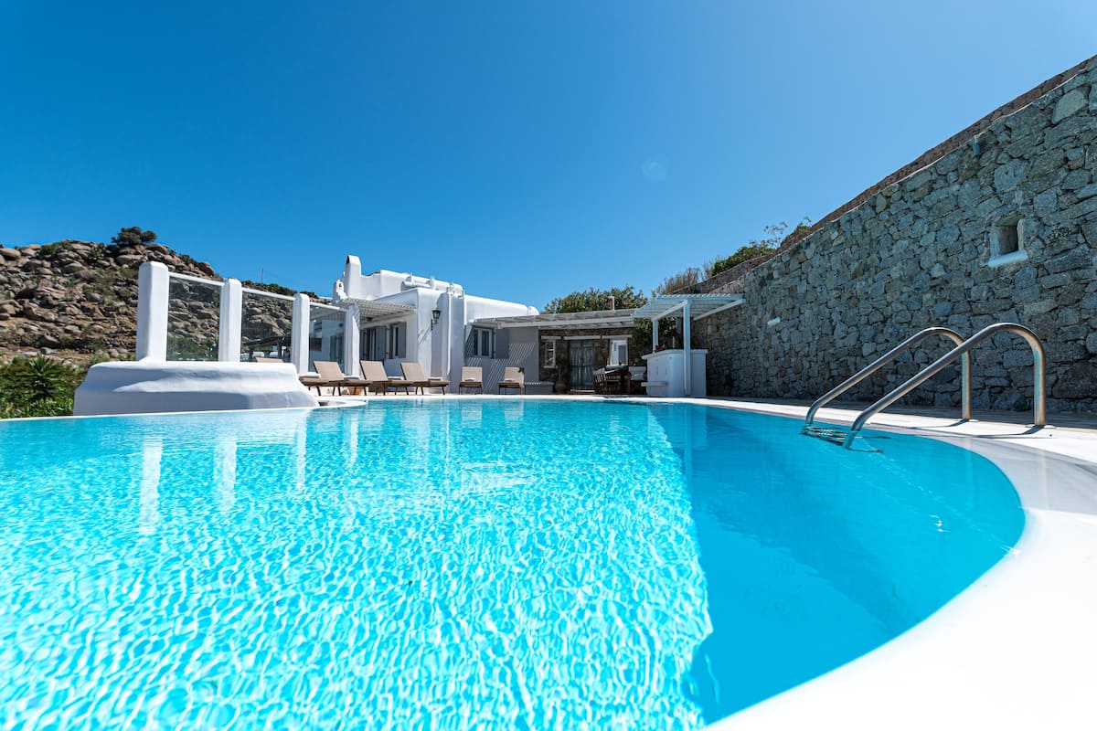 A clear blue swimming pool with lounge chairs and a stone wall.