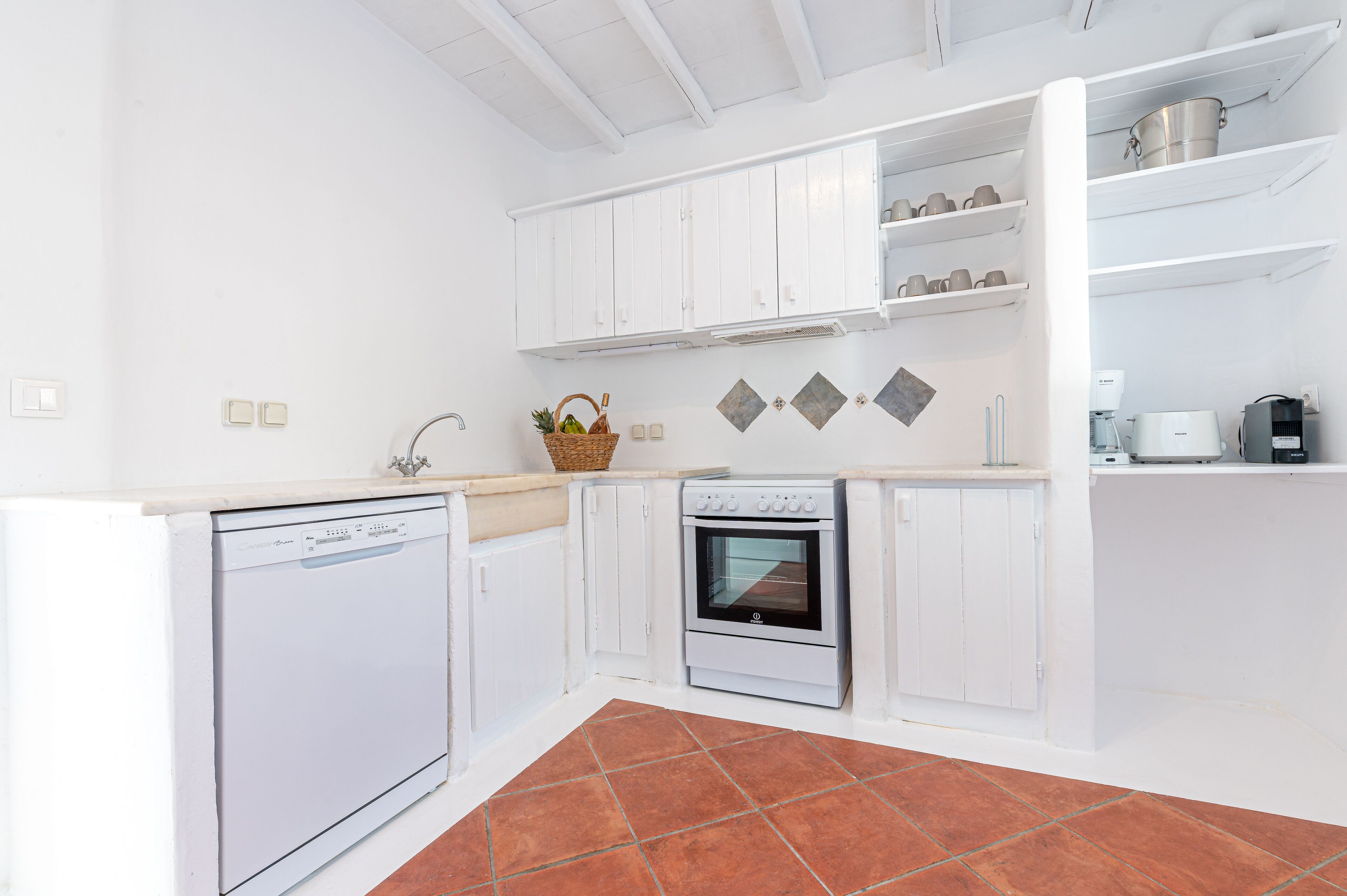 A kitchen with white cabinets, a dishwasher, an oven, and a countertop with a basket of fruit.