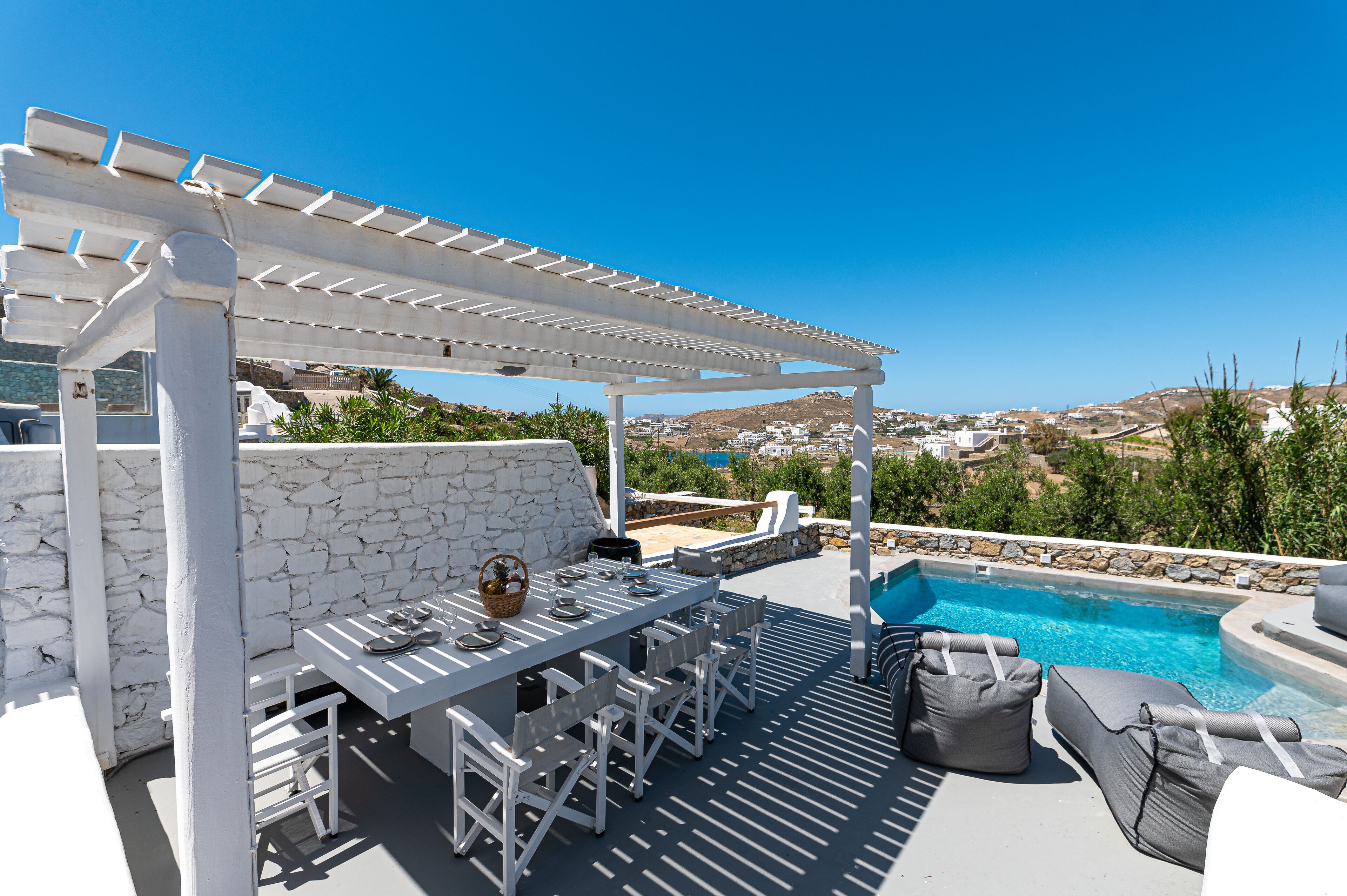 A poolside area with a pergola, white stone wall, and a view of the landscape.