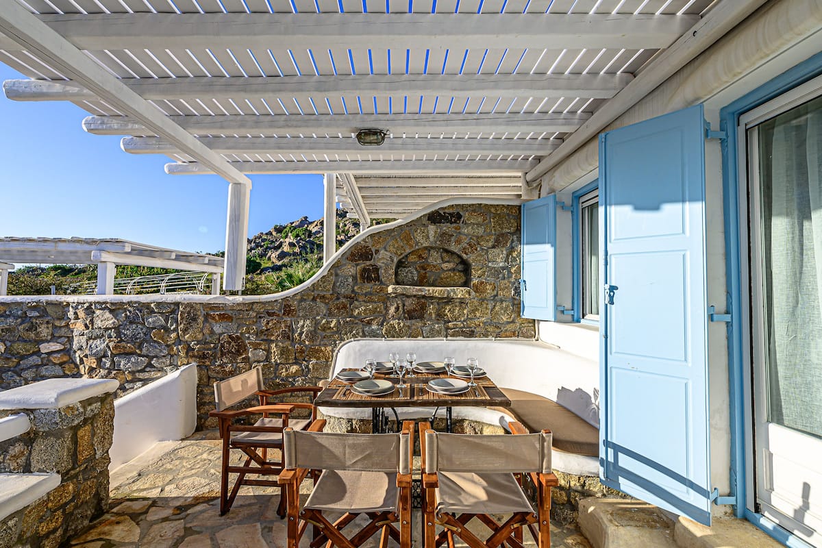An outdoor dining area with stone walls, a pergola, and a stone fireplace.