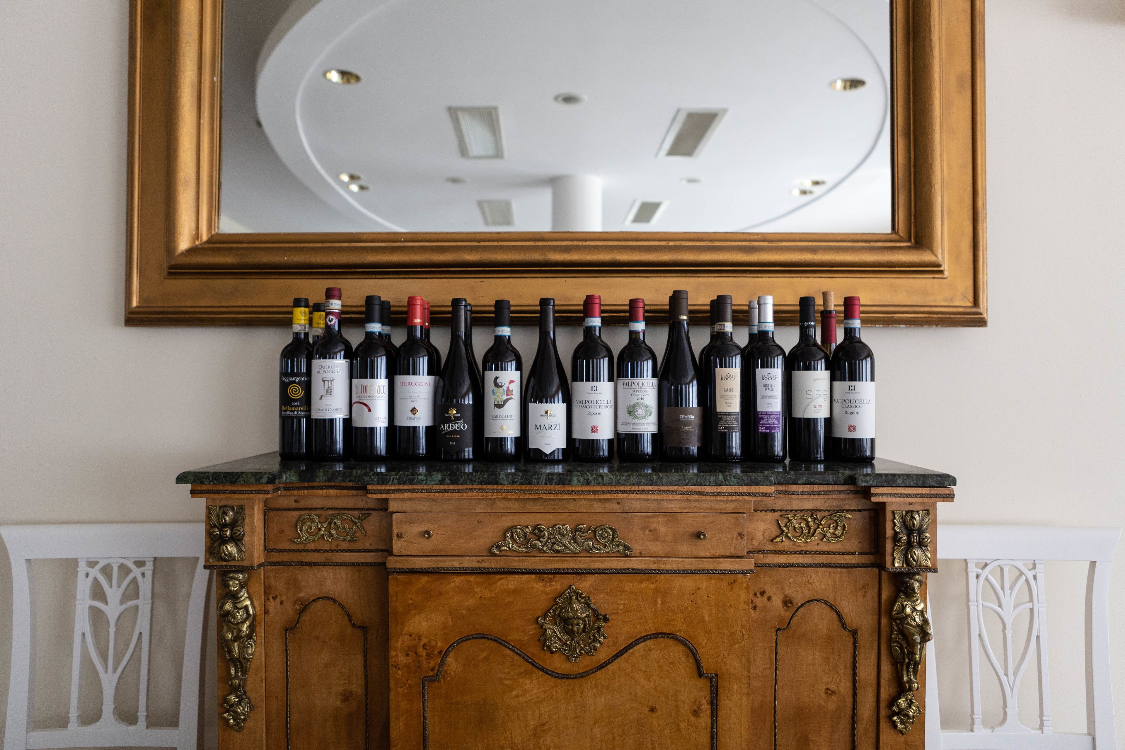 Un armario de madera con un espejo encima, mostrando una fila de botellas de vino.
