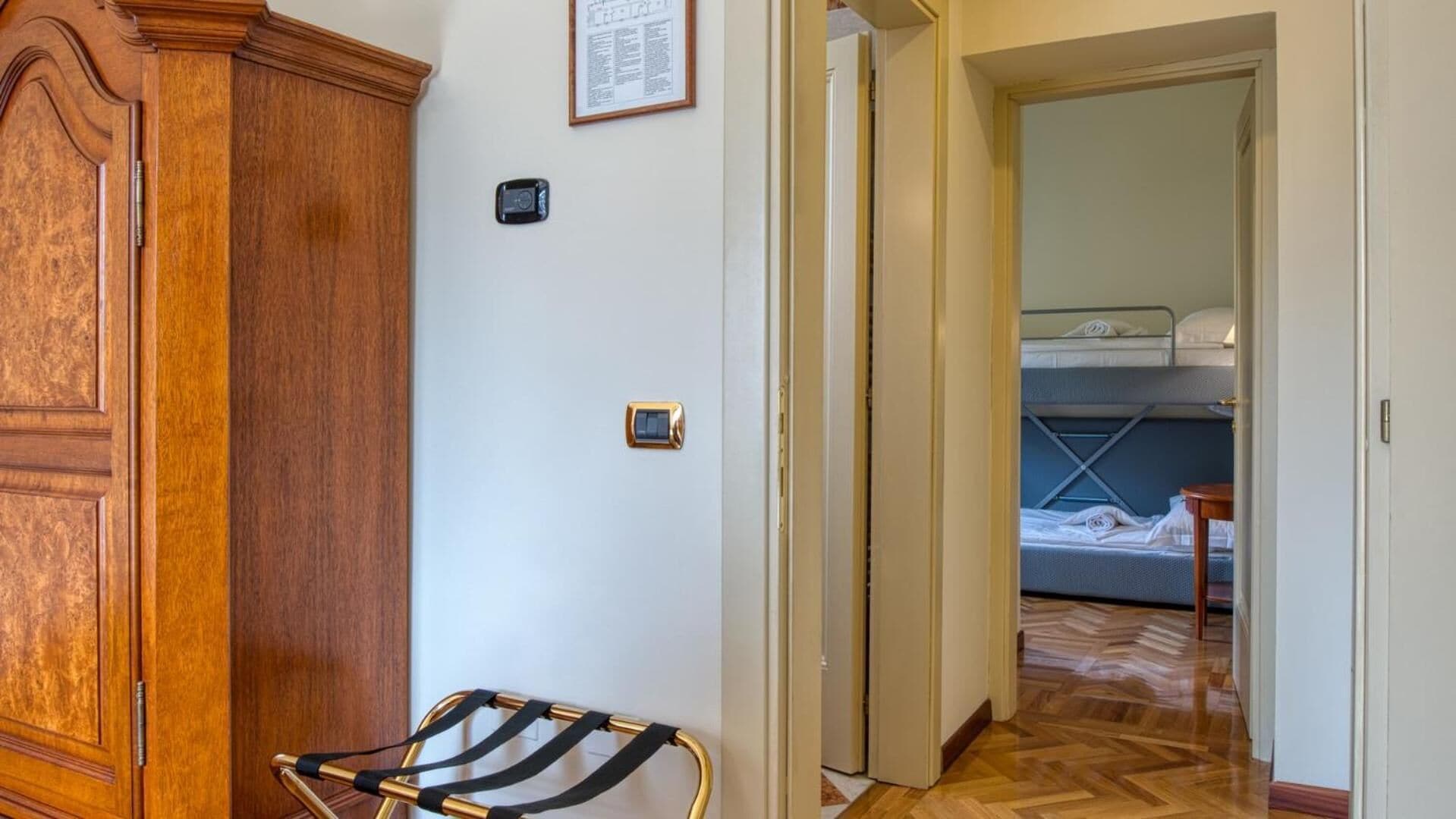 A room with a wooden wardrobe, a small table, and a bunk bed with a mattress and pillows.