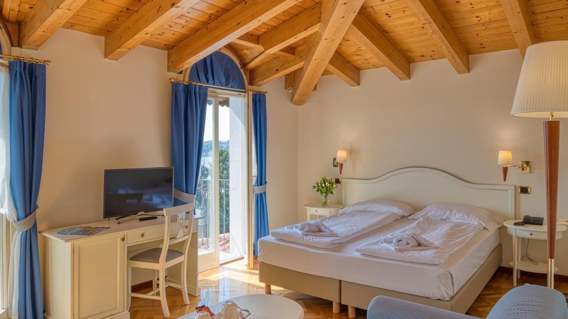 A bedroom with a bed, a desk, a television, and a window with curtains.