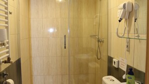 A bathroom with a glass-enclosed shower, a toilet with a towel on top, a sink, and a hairdryer mounted on the wall.
