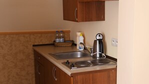 A small kitchen with wooden cabinets, a sink, a kettle, and a bottle of dish soap.