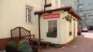 A small reception area with a wooden bench and a table, a sign reading "RECEPTJA", and potted plants.