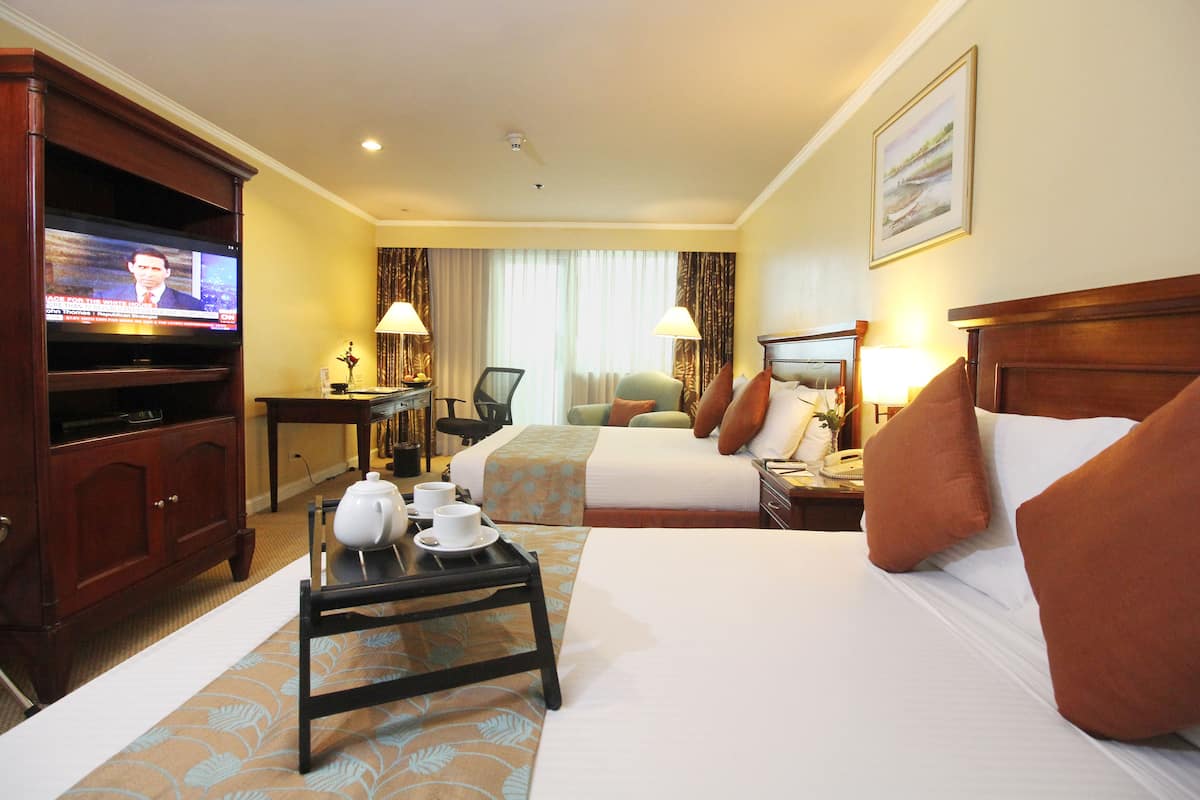 A hotel room with two beds, a television, a desk with a lamp, and a coffee tray.