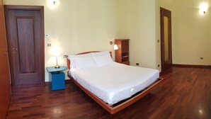 A bedroom with a wooden bed, a nightstand with a lamp, a blue dresser, and a wooden wardrobe. - B&B Il Roma (Sulmona)