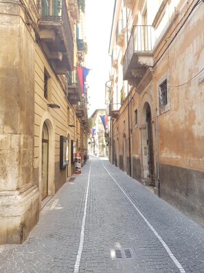 A cobblestone street flanked by historic buildings with balconies and arched doorways.