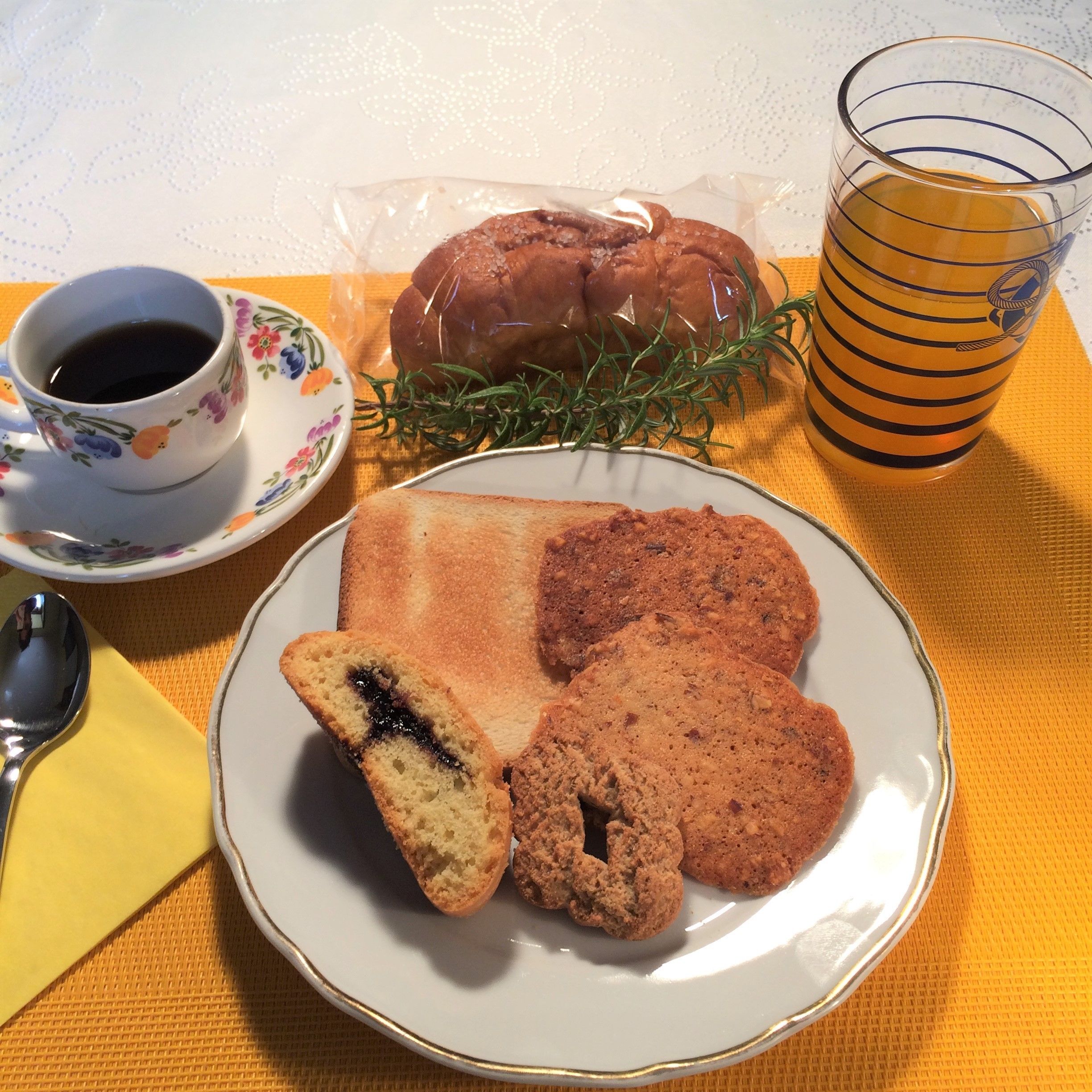 A plate with pastries, a cup of coffee, and a glass of orange juice on a table.