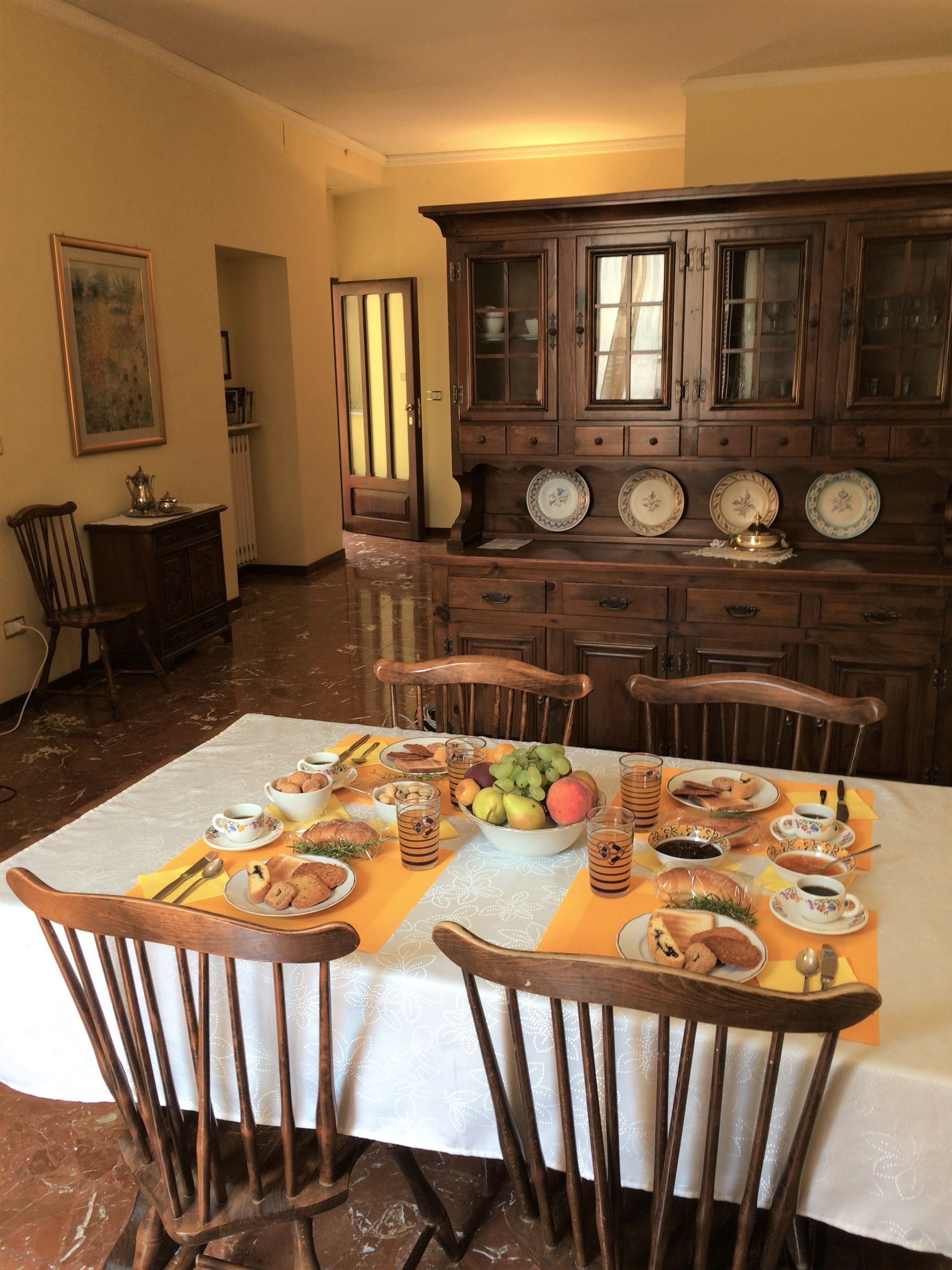 A dining area with a table set for four, surrounded by wooden chairs. A wooden cabinet with glass doors is in the background.