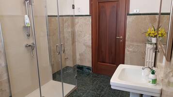 A bathroom with a glass-enclosed shower, a wooden door, a sink with a mirror, and a flower vase.