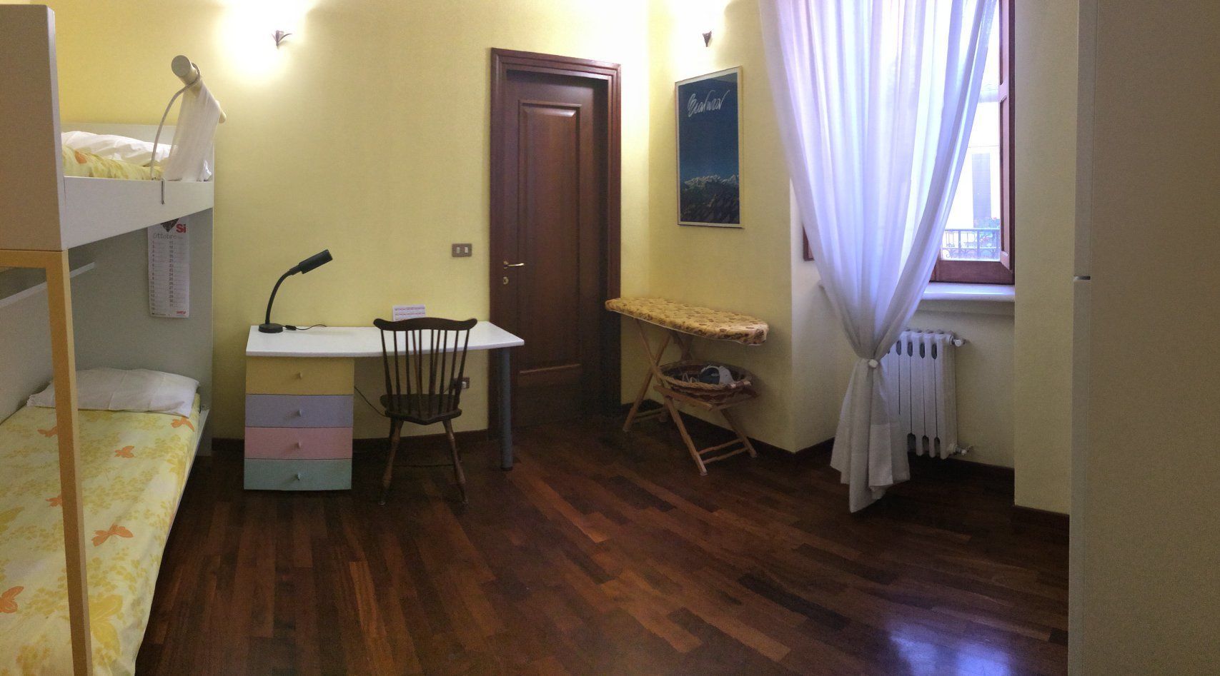 Una habitación con literas, un escritorio con silla, un radiador y una ventana con cortinas.