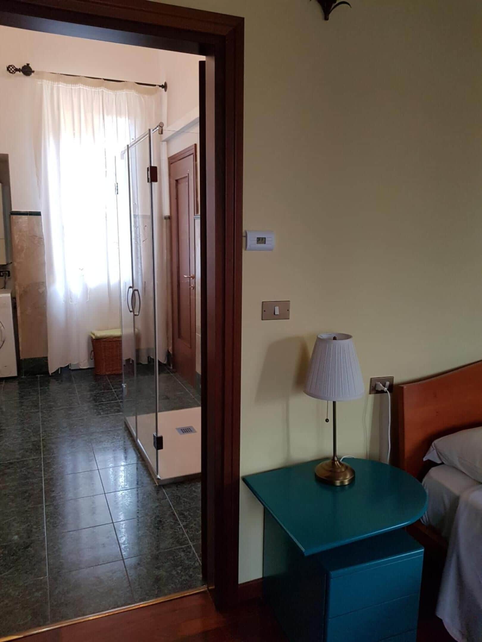 A hotel room with a bed, a nightstand, a lamp, a mirror, and a view of the bathroom and kitchen.