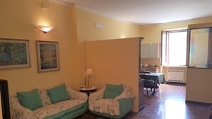 A living room with a sofa, a small table with a lamp, and a dining area with chairs and a table. - B&B Il Roma (Sulmona)