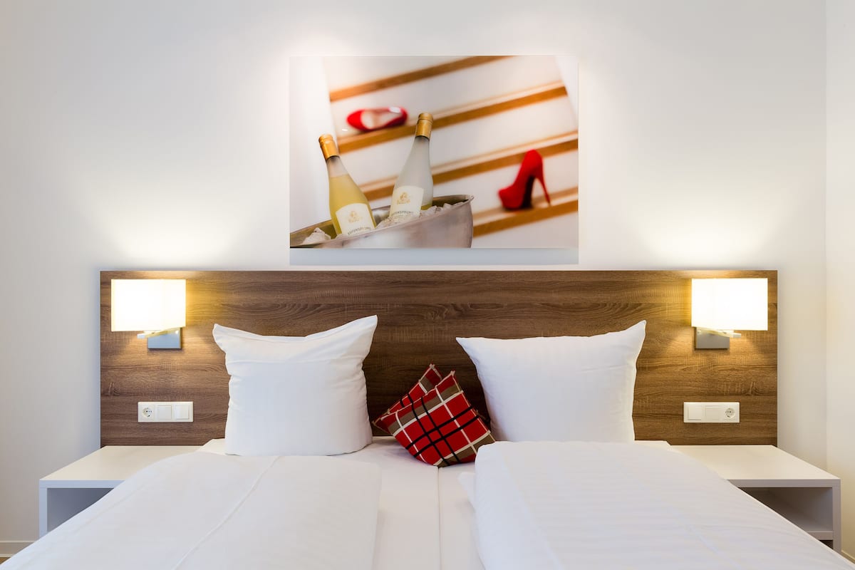 Hotellihuone, jossa on sänky, kaksi yöpöytävalaisinta, puinen sängynpääty ja sängyn yläpuolella oleva kehystetty kuva.