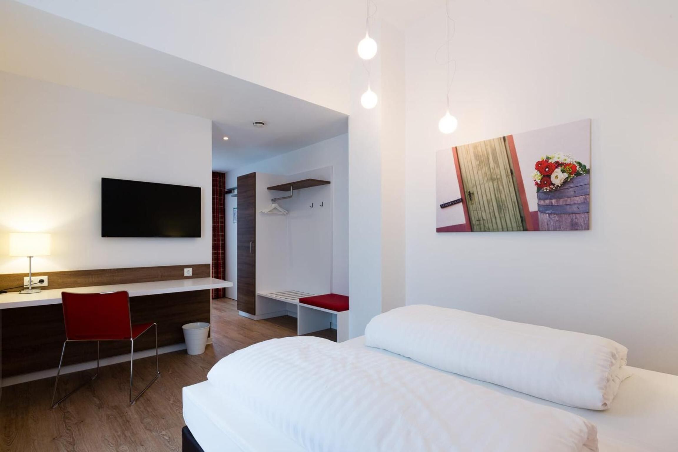 A hotel room with a bed, a desk with a chair, a TV, and a painting on the wall.