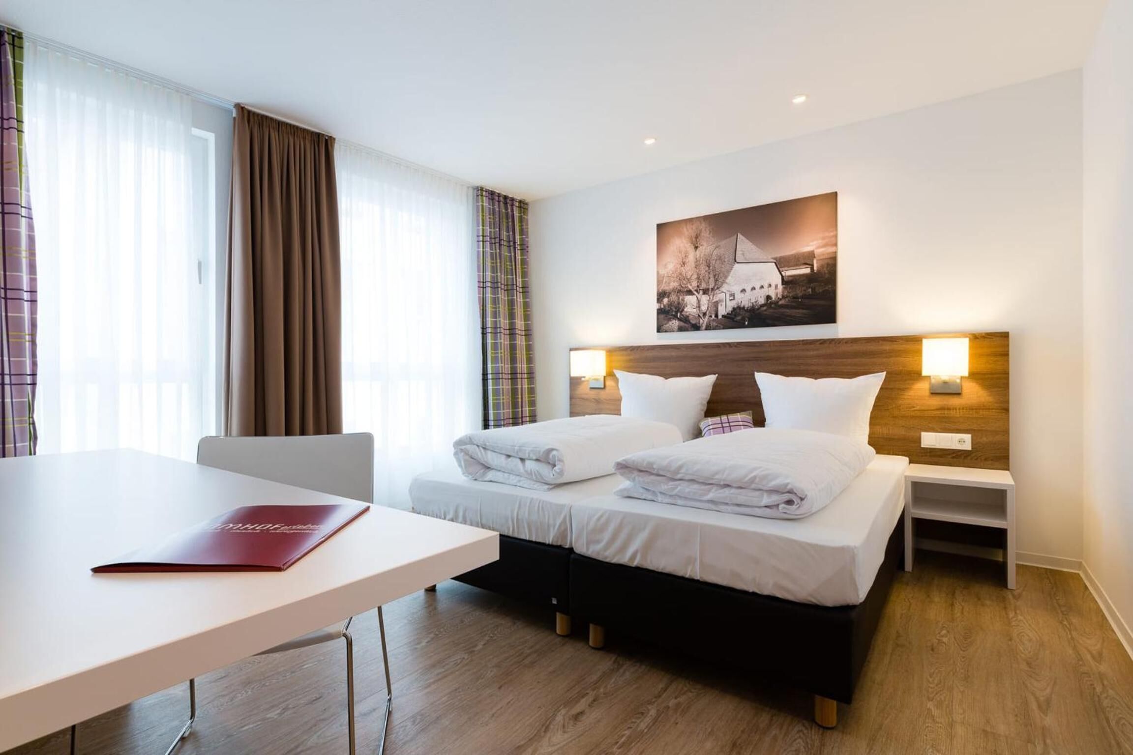 Ein Hotelzimmer mit zwei Betten, einem Schreibtisch und einem Fenster mit Vorhängen.