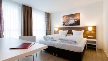 Ein Hotelzimmer mit zwei Betten, einem Schreibtisch und einem Fenster mit Vorhängen.