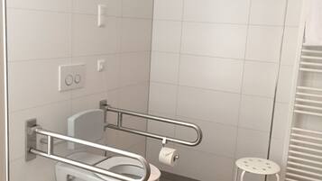 A modern bathroom with a white toilet, a handrail, a small stool, and a towel rack.