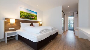 A modern bedroom with a large bed, wooden flooring, and a painting of a vineyard on the wall. - Schlafgut Domhof (Guntersblum)
