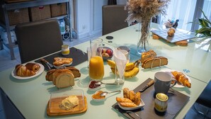 Une table à manger dressée avec des aliments pour le petit-déjeuner, notamment des croissants, du pain, des bananes et du jus de fruits.